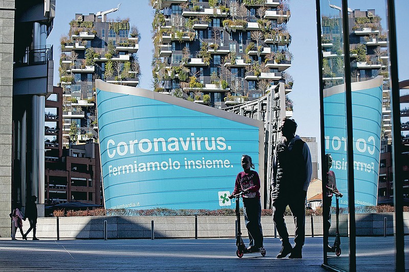 FILE - In this March 11, 2020, file photo, a man and a girl on a scooter are backdropped by a Lombardy region campaign advertising reading in Italian ' Coronavirus let's stop it together ', at the Porta Nuova business district in Milan. Italy closed shops and restaurants after locking down in the face of 10,000 reported infections. (AP Photo/Luca Bruno, File)