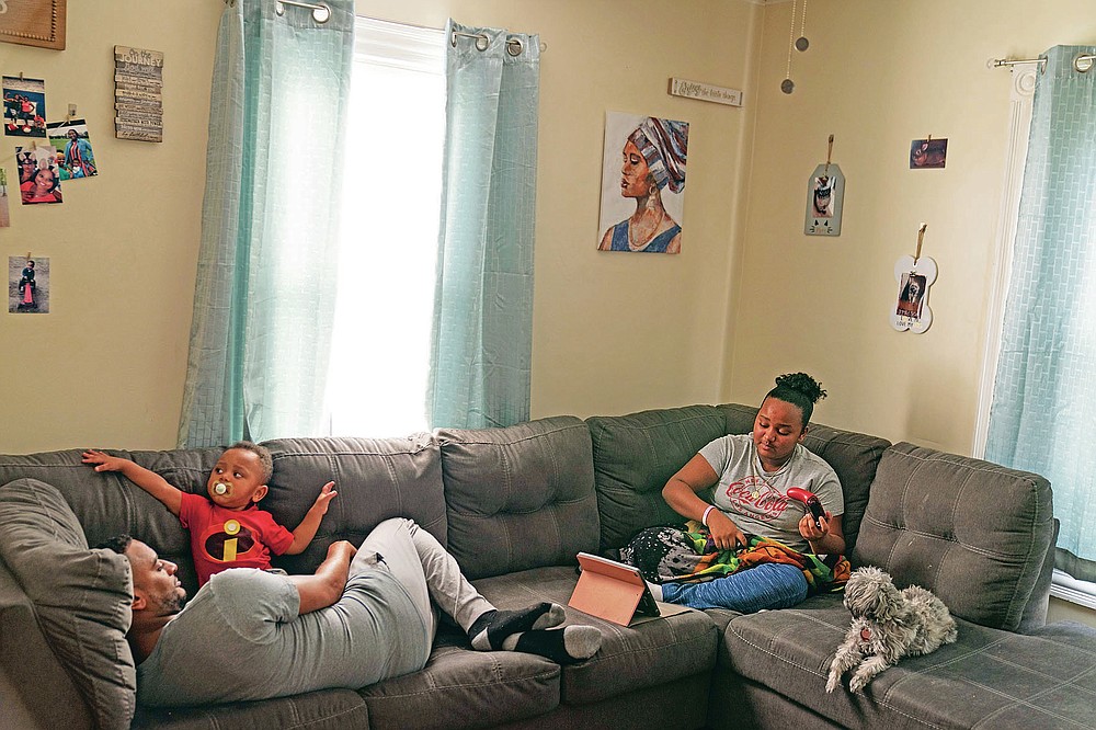 Darelyn Maldonado, 12, right, sits on the couch with her dog, Lisa, stepfather, Steven Depina, left, and 16-month-old brother, Elijah, at their home in Pawtucket, R.I., Wednesday, March 3, 2021. Maldonado, a seventh grade student, has been out of in person school for a year since the pandemic began. She feels like she's lost friends over the past year, has missed out on playing softball which she loves and just wants her life to go back to normal. (AP Photo/David Goldman)