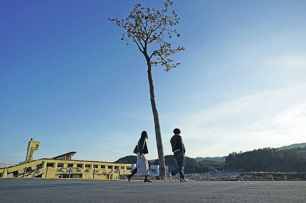 A man and a woman walk near a replica of a lone pine tree that initially survived the 2011 tsunami that flattened the surrounding coastal forest, in Rikuzentakata, Iwate Prefecture, northern Japan Thursday, March 4, 2021. The tree, which eventually died of seawater exposure, was known as the "Miracle Pine," and townspeople treated, reinforced and then preserved it as a memorial and symbol of hope for the region. (AP Photo/Eugene Hoshiko)