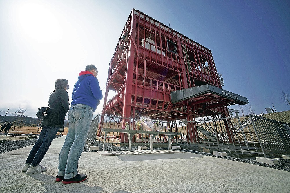 Visitors look at the skeleton of the disaster prevention headquarters building, where 43 workers died as the March 11, 2011 tsunami washed over it, in Minamisanriku, Miyagi Prefecture, northern Japan, Saturday, March 6, 2021. The three-story building is one of legacies that still stand in northern Japan's coastal towns, 10 years after the earthquake and tsunami that killed more than 18,000 people. (AP Photo/Eugene Hoshiko)