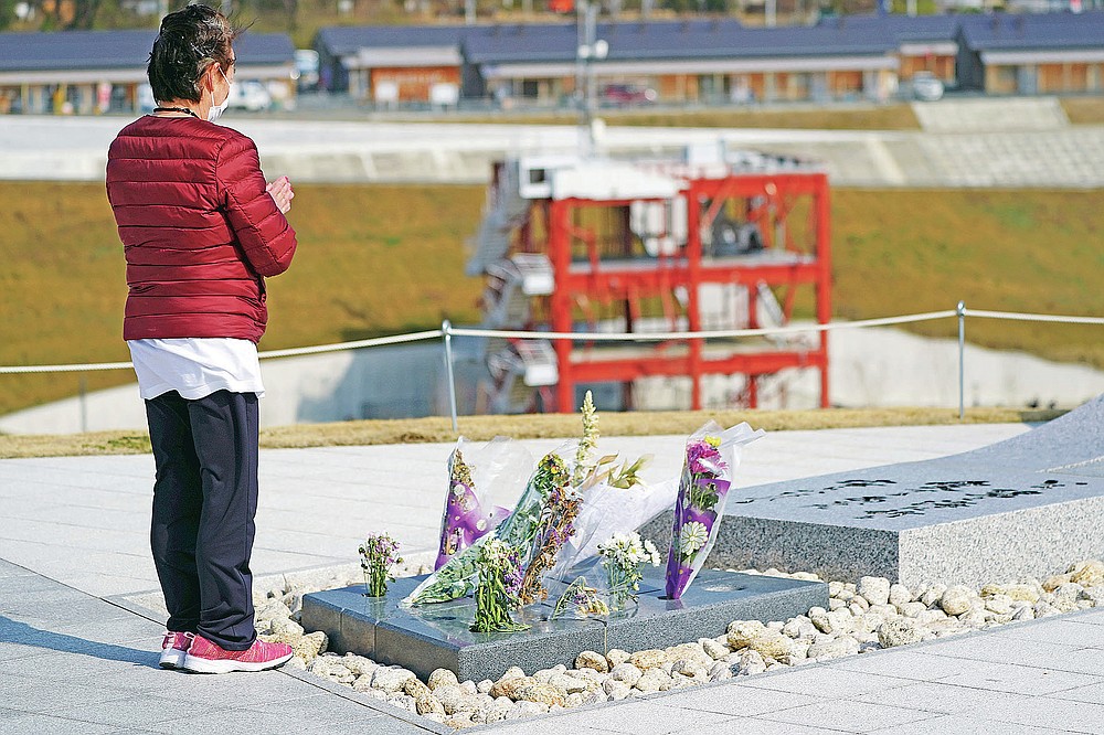 A visitor prays for the victims of the 2011 tsunami near the skeleton of the tsunami-damaged disaster prevention headquarters, where 43 workers died as the tsunami washed over it, in Minamisanriku, Miyagi Prefecture, northern Japan, Saturday, March 6, 2021. The three-story building is one of legacies that still stand in northern Japan's coastal towns, 10 years after the earthquake and tsunami that killed more than 18,000 people. (AP Photo/Eugene Hoshiko)