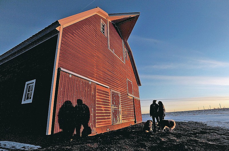 Hans Madsen Matt and Libby Mitchell stand next to their restored barn Tuesday morning, Jan. 5, 2021, as the sun rises in the east in Duncombe, Iowa.  The barn was moved from a nearby farm one year ago and the couple have now completed the exterior work. They'll start on the interior in the spring.  (Hans Madsen/The Messenger via AP)