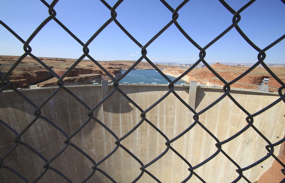 This Aug. 21, 2019 image shows Glen Canyon Dam beyond a chainlink fence near Page, Arizona. A plan by Utah could open the door to the state pursuing an expensive pipeline that critics say could further deplete the lake, which is a key indicator of the Colorado River's health. (AP Photo/Susan Montoya Bryan)