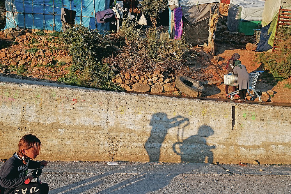 Children play as others put water on a shopping cart outside the perimeter of the overcrowded refugee camp at the port of Vathy on the eastern Aegean island of Samos, Greece, Tuesday, Feb. 23, 2021. On a hill above a small island village, the sparkling blue of the Aegean just visible through the pine trees, lies a boy’s grave. His first ever boat ride was to be his last - the sea claimed him before his sixth birthday. His 25-year-old father, like so many before him, had hoped for a better life in Europe, far from the violence of his native Afghanistan. But his dreams were dashed on the rocks of Samos, a picturesque Greek island almost touching the Turkish coast. Still devastated from losing his only child, the father has now found himself charged with a felony count of child endangerment. (AP Photo/Thanassis Stavrakis)