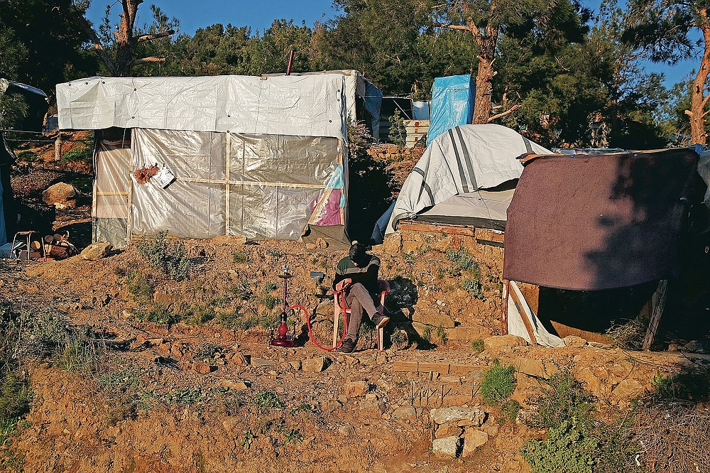 A migrant sitting next to makeshift tents, smokes, outside the perimeter of the overcrowded refugee camp at the port of Vathy on the eastern Aegean island of Samos, Greece, Tuesday, Feb. 23, 2021. On a hill above a small island village, the sparkling blue of the Aegean just visible through the pine trees, lies a boy’s grave. His first ever boat ride was to be his last - the sea claimed him before his sixth birthday. His 25-year-old father, like so many before him, had hoped for a better life in Europe, far from the violence of his native Afghanistan. But his dreams were dashed on the rocks of Samos, a picturesque Greek island almost touching the Turkish coast. Still devastated from losing his only child, the father has now found himself charged with a felony count of child endangerment. (AP Photo/Thanassis Stavrakis)