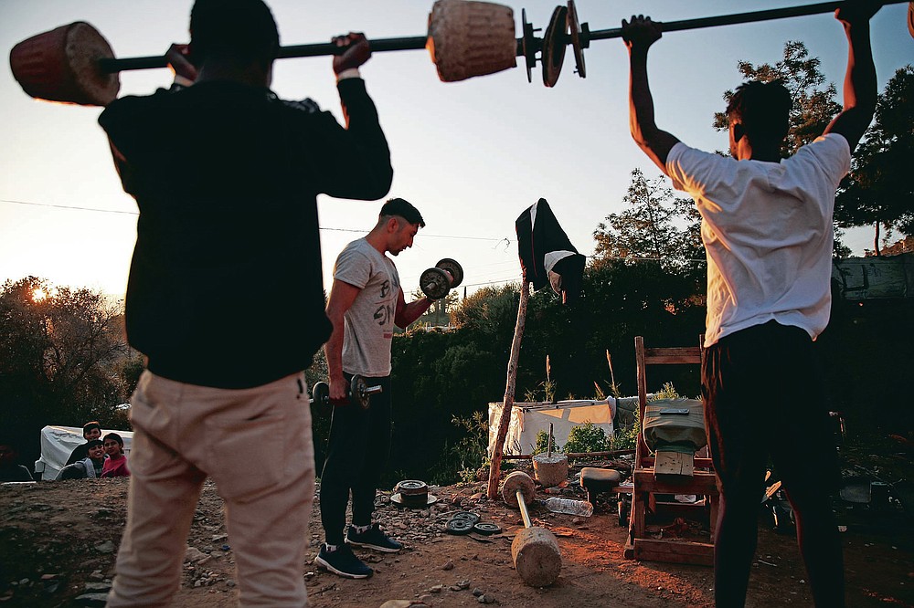 Migrants lift weights at a makeshift gym outside the perimeter of the overcrowded refugee camp at the port of Vathy on the eastern Aegean island of Samos, Greece, Tuesday, Feb. 23, 2021. On a hill above a small island village, the sparkling blue of the Aegean just visible through the pine trees, lies a boy’s grave. His first ever boat ride was to be his last - the sea claimed him before his sixth birthday. His 25-year-old father, like so many before him, had hoped for a better life in Europe, far from the violence of his native Afghanistan. But his dreams were dashed on the rocks of Samos, a picturesque Greek island almost touching the Turkish coast. Still devastated from losing his only child, the father has now found himself charged with a felony count of child endangerment. (AP Photo/Thanassis Stavrakis)