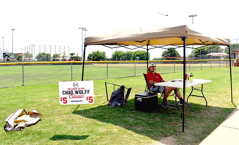 MARK HUMPHREY  ENTERPRISE-LEADER/Dalton Cook, a 2020 Siloam Springs graduate, brought his own canopy which provided shade for manning the gate last week during the Chad Wolff Classic baseball tournament at the Farmington Sports Complex on Southwinds Drive. Temperatures hit triple digits during the tourney.