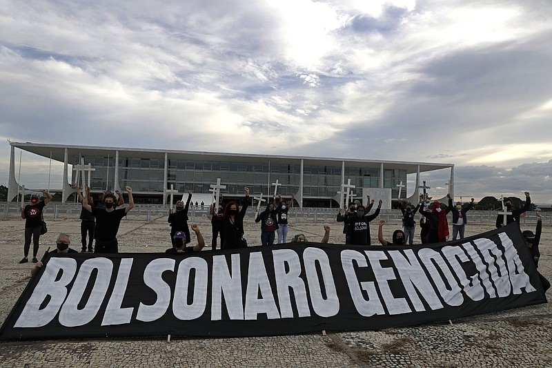Demonstrators hold crosses to represent people who have died of COVID-19 behind the Portuguese phrase "Bolsonaro genocide" as they protest the president's handling of the COVID-19 pandemic outside Planalto presidential palace in Brasilia, Brazil, Friday, March 19, 2021. (AP Photo/Eraldo Peres)