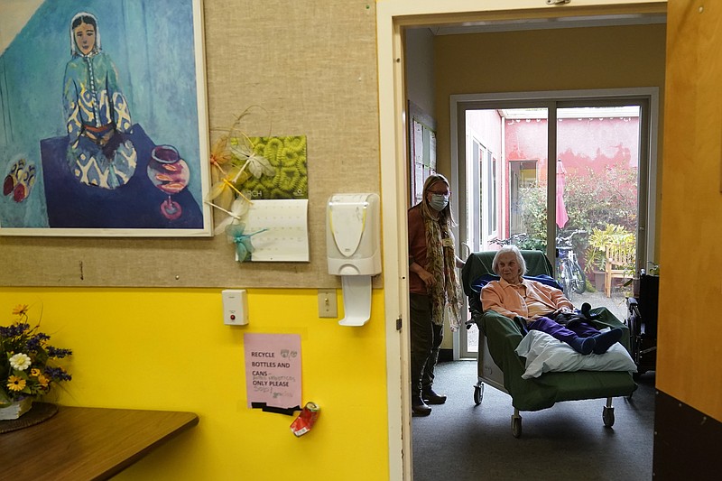 Chaparral House activities director Erika Shaver-Nelson, left, stands next to resident Connie in the hallway at Chaparral House in Berkeley, Calif., Thursday, March 18, 2021. Nursing homes and other elderly residences battered by COVID-19 are easing lockdown-like restrictions more than a year into the pandemic. (AP Photo/Jeff Chiu)