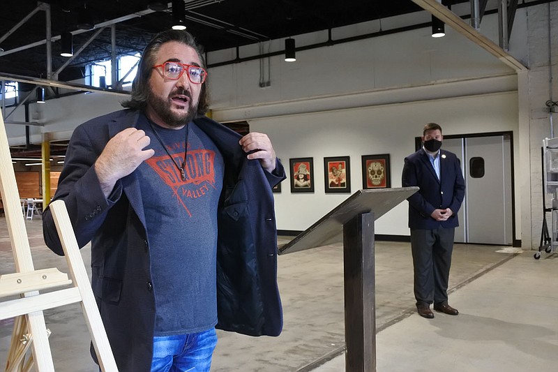 Brandon Goldsmith, executive director of the River Valley Film Society, left, displays a shirt that states "River Valley Strong" while speaking at a news conference and check-giving ceremony at the Bakery District in Fort Smith on Thursday as Fort Smith Vice Mayor and Ward 1 City Director Jarred Rego, right, listens. Arvest Bank - Fort Smith will sponsor the nonprofit organization's Fort Smith International Film Festival with a $10,000 donation. The inaugural event will take place Aug. 13-14. 
(NWA Democrat-Gazette/Thomas Saccente)