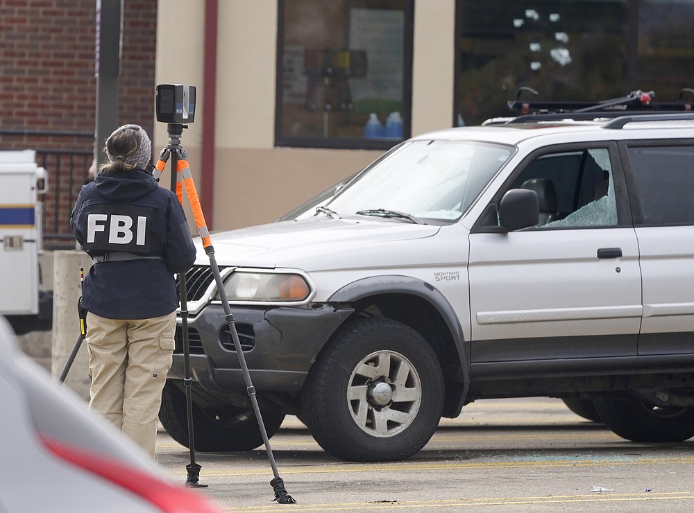 An investigator from the FBI collects evidence near a sports-utility vehicle with a windshield and side window damaged by gunfire sitting in the parking lot of a King Soopers grocery store Thursday, March 25, 2021, in Boulder, Colo. Ten people were killed in a mass shooting at the supermarket on Monday. (AP Photo/David Zalubowski)