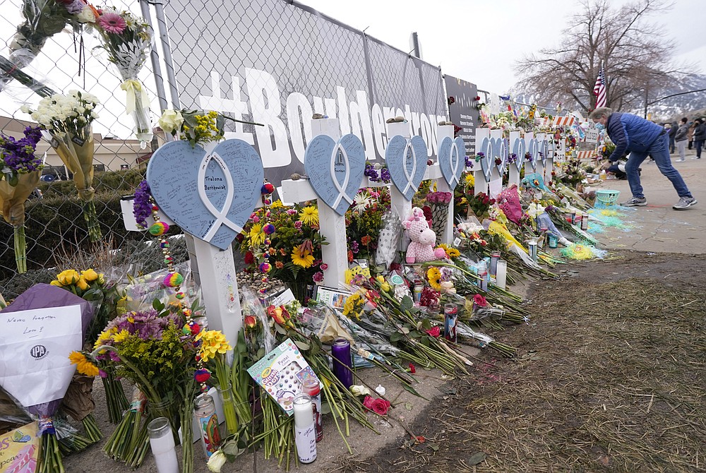 Clint Cooper places a tribute to the victims amid the crosses put up along the temporary fence around the parking lot of a King Soopers grocery store Thursday, March 25, 2021, in Boulder, Colo. Ten people were killed in a mass shooting at the supermarket on Monday. (AP Photo/David Zalubowski)