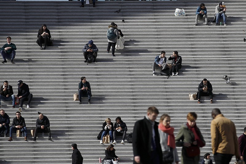 People walk and take a rest at the business district of La Defense outside Paris on March 12, 2020. Some European countries have started to welcome vaccinated travelers, including American tourists; others are making preparations to ease restrictions in time for the summer season. But France, along with Belgium and Portugal, has reintroduced measures that restrict nonessential travel. (AP/Christophe Ena)