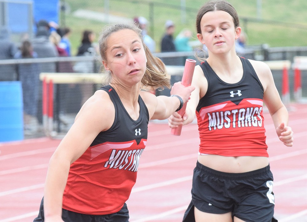 RICK PECK/SPECIAL TO MCDONALD COUNTY PRESS McDonald County's Kaycee Factor gets a hand-off from teammate Madison Burton on the way to a third place finish in the 4x800 relay at the Stancell McDonald County Stampede held on March 25, at McDonald County High School. Others on the relay were Anna Belle Price and Melysia McCrory.