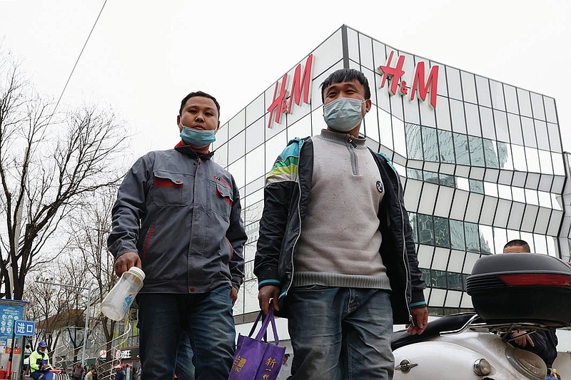 Workers wearing masks pass by an H&M store in Beijing on Monday, March 29, 2021. China stepped up pressure Monday on foreign shoe and clothing brands to reject reports of abuses in Xinjiang, telling companies that are targeted by Beijing for boycotts to look more closely and pointing to a statement by one that it found no forced labor. (AP Photo/Ng Han Guan)