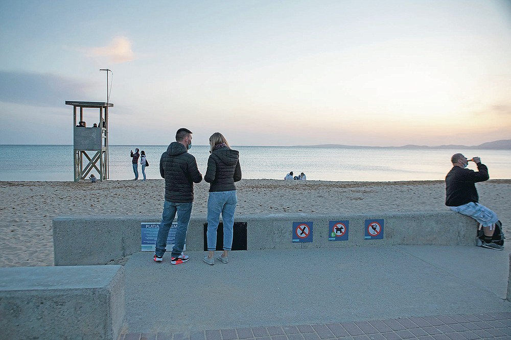 Tourists stand on a beach during sunset at the Spanish Balearic Island of Mallorca, Spain, Saturday, March 27, 2021. Efforts in Spain to restart tourism activity is drawing a mixed picture due to a patchwork of national, regional and European rules on travel that is confusing both tourists and their hosts. (AP Photo/Francisco Ubilla)
