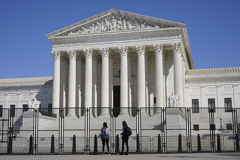 FILE - In this March 21, 2021, file photo people view the Supreme Court building from behind security fencing on Capitol Hill in Washington after portions of an outer perimeter of fencing were removed overnight to allow public access. A Supreme Court case being argued this week amid March Madness could erode the difference between elite college athletes and professional sports stars. (AP Photo/Patrick Semansky, File)