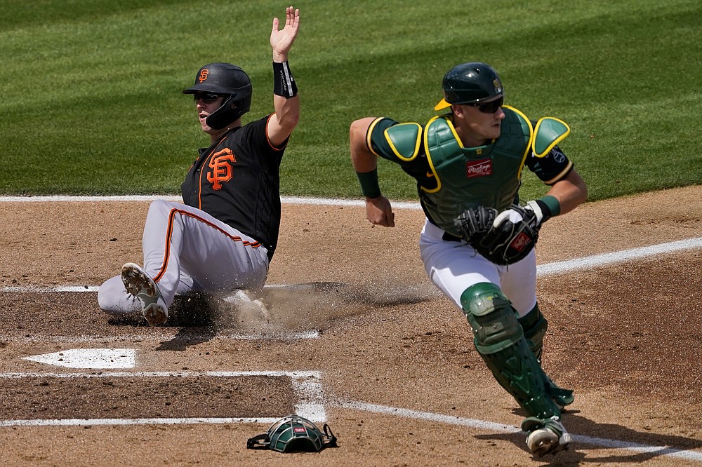 San Francisco Giants' Buster Posey scores on a base hit by teammate Mauricio Dubon as Oakland Athletics catcher Sean Murphy waits for the throw during the first inning of a spring training baseball game, Monday, March 29, 2021, in Mesa, Ariz. (AP Photo/Matt York)