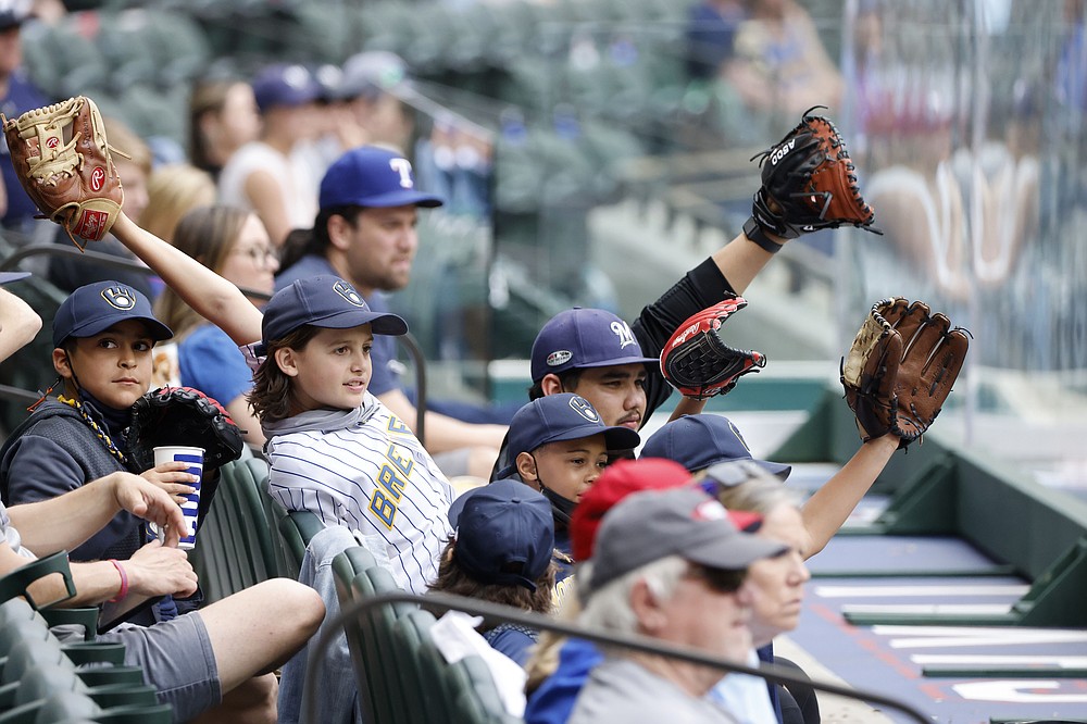 Milwaukee Brewers fans try to get a players attention from behind protective plexi-glass during a preseason baseball game against the Texas Rangers, Tuesday, March 30, 2021, in Arlington, Texas. (AP Photo/Michael Ainsworth)