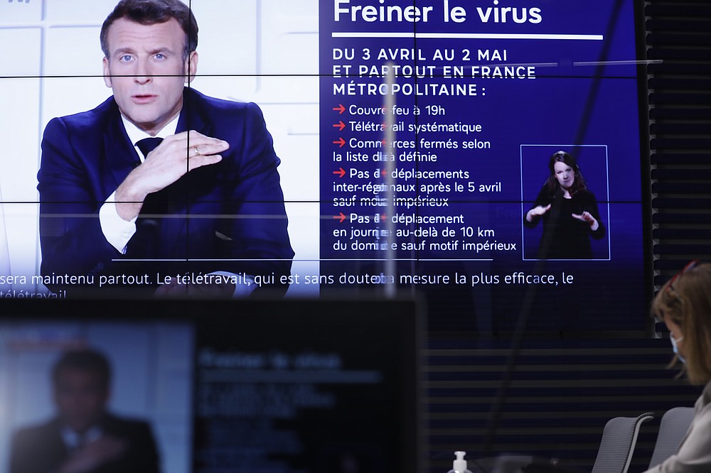 Local prefect Josiane Chevalier, right, watches French President Emmanuel Macron addressing the nation, in the local government building in Strasbourg, eastern France, Wednesday, March 31, 2021. French President Macron announced 3-week nationwide school closure, domestic travel ban amid virus surge. Title reads: Slowing down the virus. (AP Photo/Jean-Francois Badias)