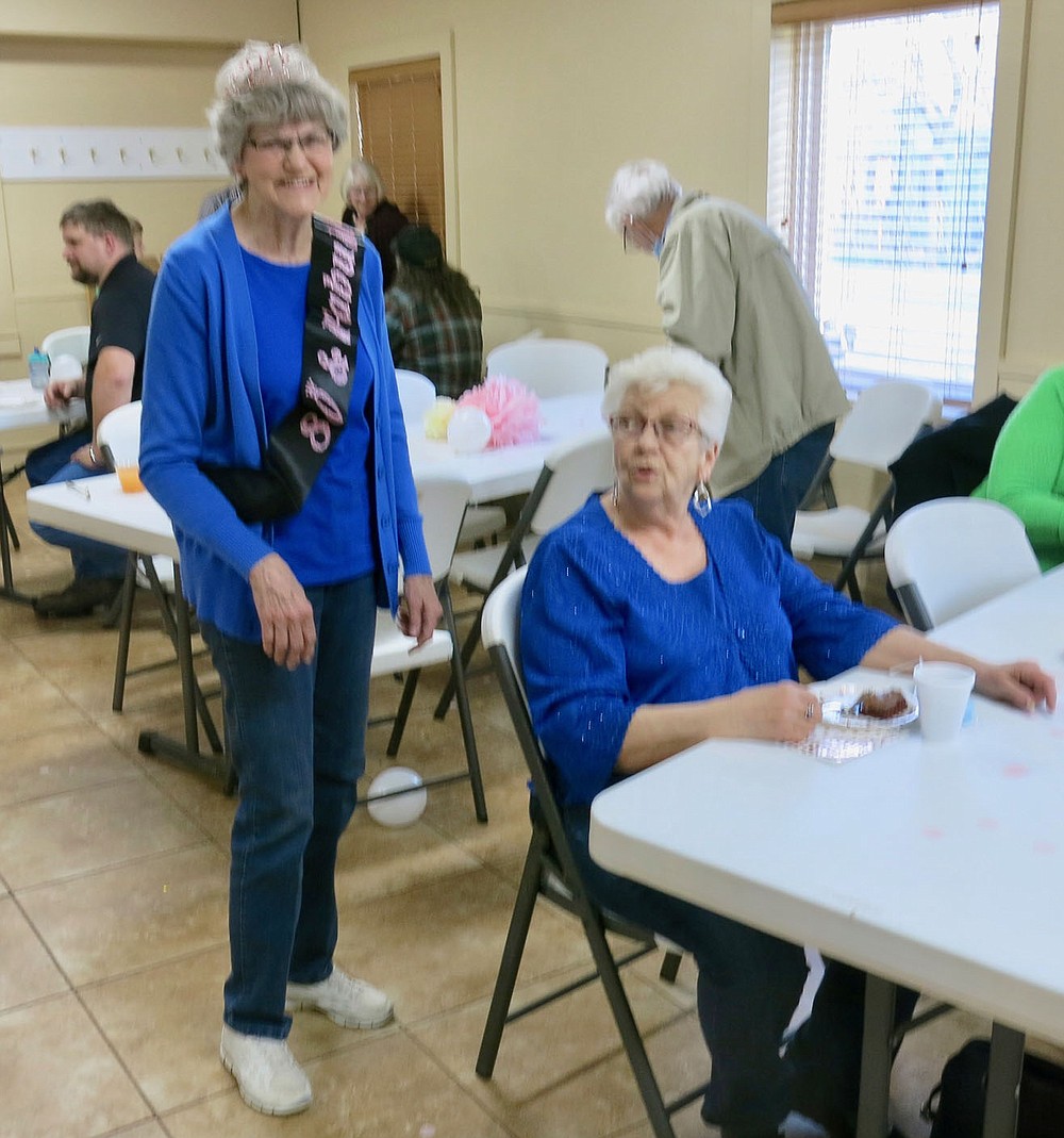 Westside Eagle Observer/SUSAN HOLLAND
Jeanie Easley pauses while visiting with Becky Denver (seated) at her 80th birthday party Wednesday evening, March 31, at the First Baptist Church in Gravette. Jeanie thought she was just going out to eat for the evening when her daughter and son-in-law, Carla and David Bailey, took her by the church. There she found a roomful of family members and friends who had come to help her celebrate with drinks, snacks, birthday cake, flowers, cards and gifts.