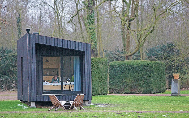 Kim Devos reads a book in a Slow Cabin in Elewijt, Belgium, Monday, Feb. 15, 2021. These Slow Cabins, set up the Belgian countryside, are the new way to vacation in pandemic times: in complete solitude and in the middle of nowhere. The wooden cabins are fully sustainable, provided you don't stay in the shower too long and you can live without Wi-Fi. (AP Photo/Virginia Mayo)