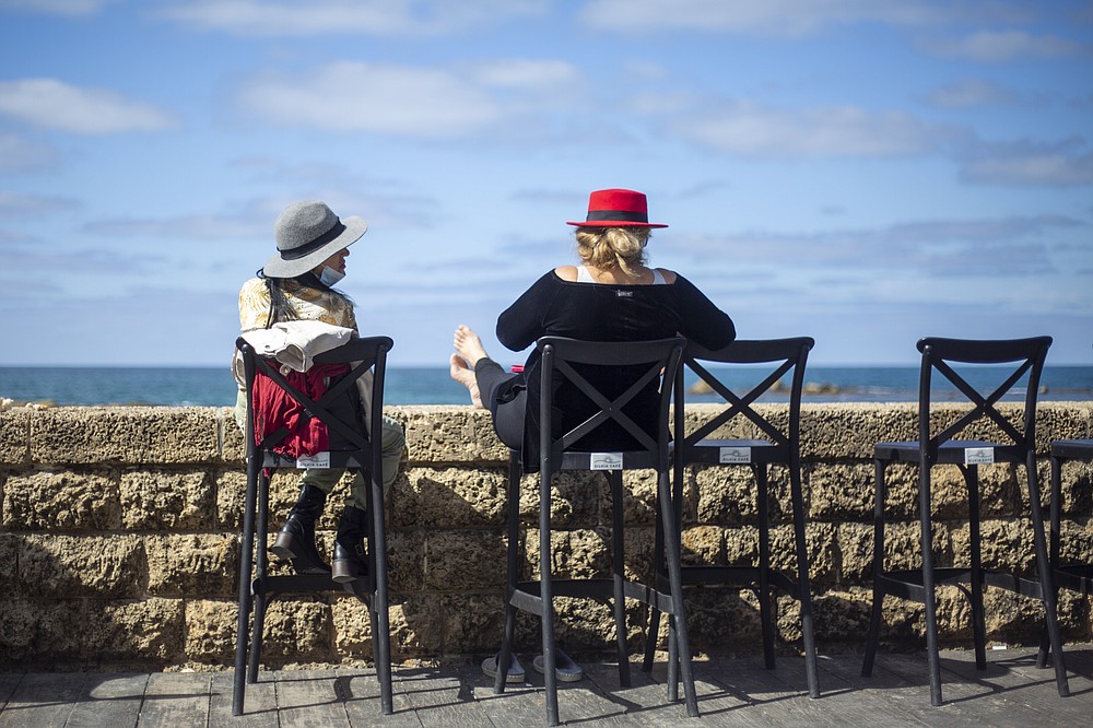 FILE - In this March 7, 2021, file photo, women sit in a caffe overlooking the Mediterranean Sea as restrictions are eased following months of government-imposed shutdowns, in Tel Aviv, Israel. While Israel provides a glimpse of what may be possible with high immunization rates, it also offers insight into the problems that lie ahead: Workplaces and schools are now grappling with what to do with those who refuse to get vaccinated. (AP Photo/Ariel Schalit, File)