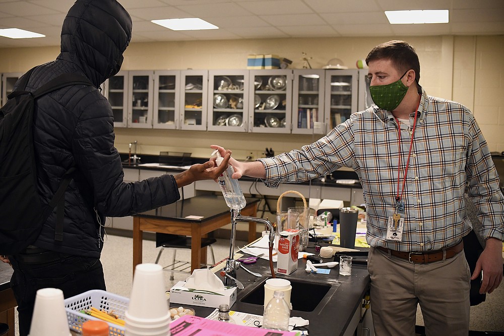 FILE - In this March 18, 2021, file photo, science teacher Christopher Duggan squirts hand sanitizer on the hands of student Jaiden Taylor, left, at Windsor Locks High School in Windsor Locks, Conn. With a massive infusion of federal aid coming their way, schools across the U.S. are weighing how to use the windfall to ease the harm of the pandemic — and to tackle problems that existed long before the coronavirus. (AP Photo/Jessica Hill, File)