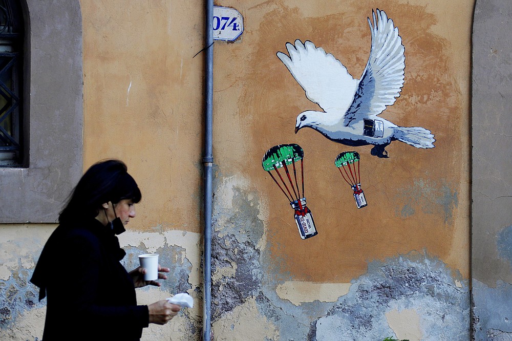 A woman walks past a mural depicting a white dove parachuting COVID-19 vaccine vials, posted near the Italian Health Ministry Headquarters in Rome, Sunday, April 4, 2021. Italy has entered a three-day strict nationwide lockdown to prevent new surges of the coronavirus. Police set up road checks to ensure people were staying close to home and extra patrols were ordered up to break up large gatherings in squares and parks, which over Easter weekend are usually packed with picnic-goers. (AP Photo/Gregorio Borgia)