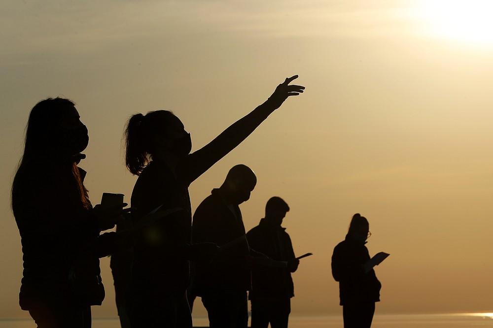 Parishioners are silhouetted against the sky as they gather and pray during an Easter sunrise service held by Park Community Church Sunday, April 4, 2021, at North Avenue Beach in Chicago. (AP Photo/Shafkat Anowar)