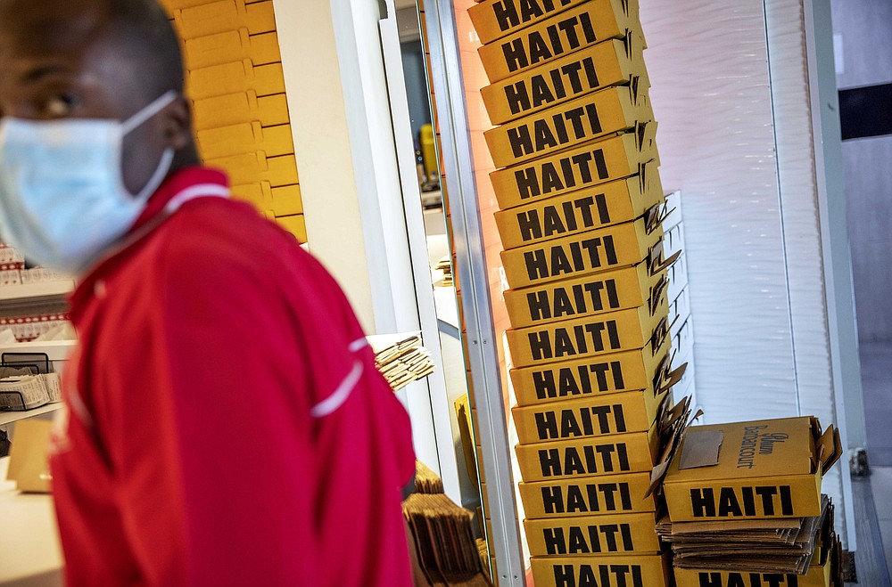 FILE - In this March 14, 2020 file photo, boxes of rum are stacked as a duty free employee wears a mask amid the COVID-19 pandemic while working at Toussaint Louverture International Airport in Port-au-Prince, Haiti. (AP Photo/David Goldman, File)