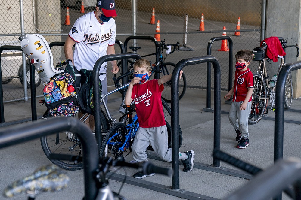 Michael Hoffman of Washington and his sons Evan, 6, center, and Andrew, 4, right, lock up their bikes as they arrive before the Washington Nationals play the Atlanta Braves in their opening day baseball game at Nationals Park, Tuesday, April 6, 2021, in Washington. (AP Photo/Andrew Harnik)