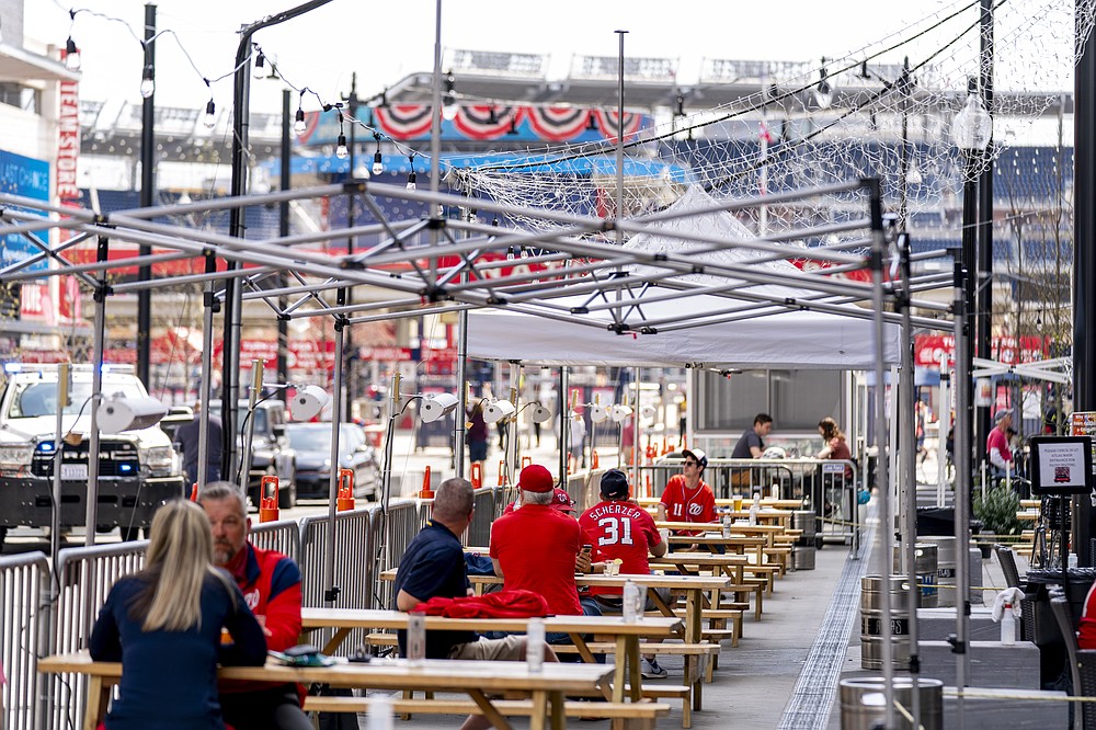 A few fans sit at outdoor bars near the centerfield gate before the Washington Nationals play the Atlanta Braves in their opening day baseball game at Nationals Park, Tuesday, April 6, 2021, in Washington. (AP Photo/Andrew Harnik)
