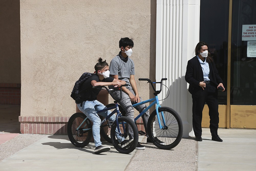 In this Monday, April 5, 2021, photo Jonathan Chilton, 14, left, sits on his BMX bike in front of the New Mexico state capitol ahead of a bill signing by the governor in Santa Fe, N.M. Chilton started school remotely on Tuesday following the Easter break. Around half of his classmates are now studying in-person, and he's not sure if he should go back with just a few weeks left in the semester. (AP Photo/Cedar Attanasio)