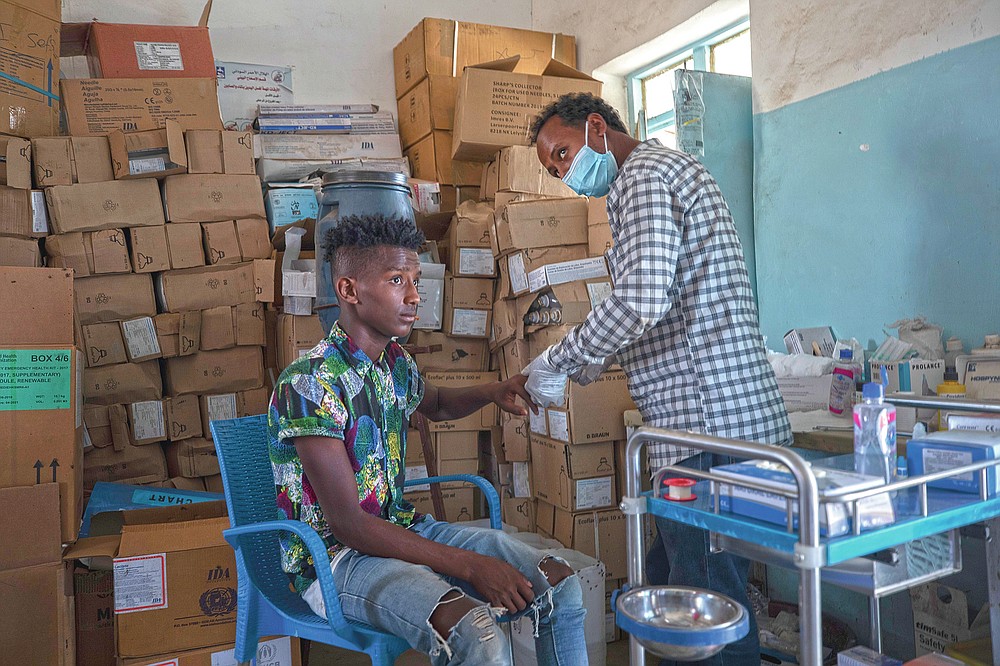 Seid Mussa Omar, a 29-year-old Tigrayan nurse from Humera, treats a man at the Sudanese Red Crescent clinic, in Hamdayet, eastern Sudan, near the border with Ethiopia, on March 17, 2021. Amhara authorities now in charge took Omar's original ID card displaying his Tigrayan ethnicity and burned it, he said. On the new card examined by the AP, traces of Tigray had vanished. It was issued in January 2021 in a city located so far north in Ethiopia that it is within sight of neighboring Eritrea. Yet the card is stamped by authorities of the Amhara region to the south. The language on the card is Amharic, not the Tigrinya of Tigray. (AP Photo/Nariman El-Mofty)