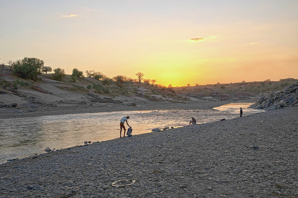 People stand on the banks of the Tekeze River, on the Sudan-Ethiopia border after Ethiopian forces blocked individuals from crossing into Sudan, near Hamdayet, eastern Sudan, on March 16, 2021. Ethiopia is at left, and Sudan is at right. (AP Photo/Nariman El-Mofty)