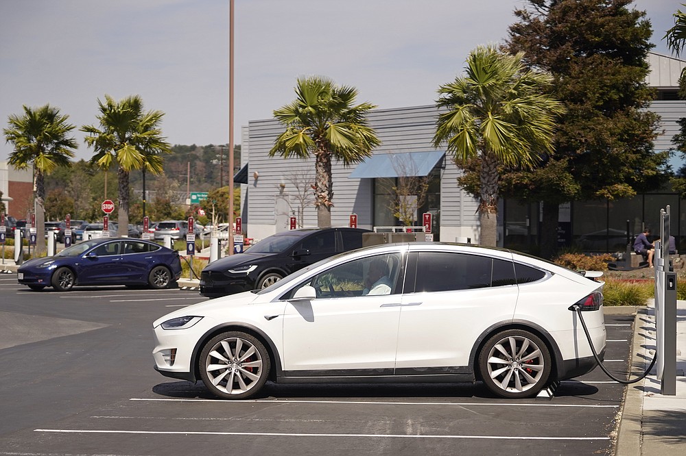 A man talks on his phone while sitting in his electric car at a Tesla charging station Friday, April 2, 2021, Marin City, Calif. The president and auto industry maintain the nation is on the cusp of a gigantic shift to electric vehicles and away from liquid-fueled cars, but biofuels producers and some of their supporters in Congress aren't buying it and argue now is the time to increase sales of ethanol and biodiesel, not abandon them. (AP Photo/Eric Risberg)