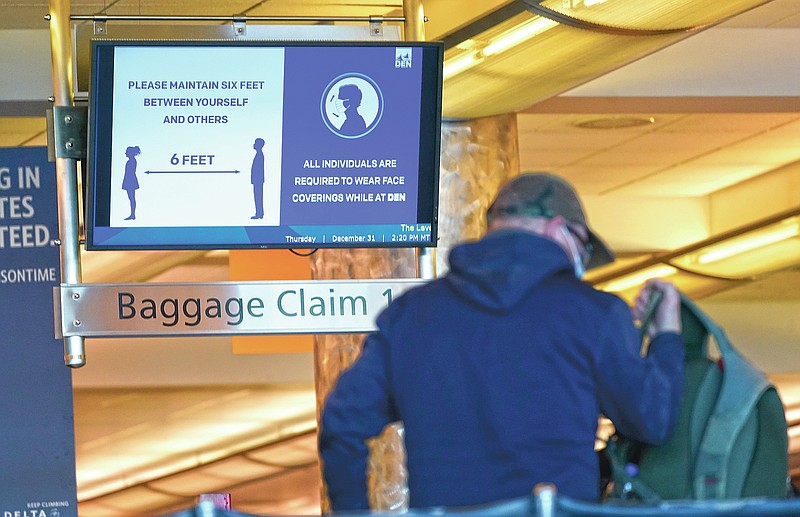 FILE - In this Thursday, Dec. 31, 2020 file photo, an electronic sign advises travelers to wear face masks and practice social distancing while passing through the main terminal of Denver International Airport in Denver. On Friday, April 9, 2021, The Associated Press reported on stories circulating online incorrectly asserting the federal government wants to require Americans to present a health passport or vaccine certificate “on demand,” including for domestic travel. While private businesses are considering vaccine passports for certain activities, Biden administration officials have said the federal government will not mandate vaccine passports. (AP Photo/David Zalubowski)