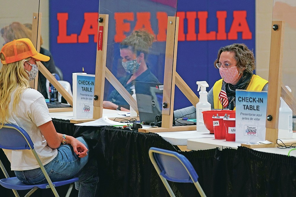 FILE - In this Tuesday, Nov. 3, 2020 file photo, an election judge checks in a voter at the La Familia Recreation Center in the Baker neighborhood south of downtown Denver. On Friday, April 9, 2021, The Associated Press reported on stories circulating online incorrectly asserting Major League Baseball had moved the All-Star game to Colorado because Georgia now requires an ID to vote, and yet Colorado also requires voter ID. But Colorado does not require an identification card to vote. Furthermore, Georgia already had a voter photo ID requirement, new sweeping rules include ID requirements to apply for a mailed ballot. (AP Photo/David Zalubowski)