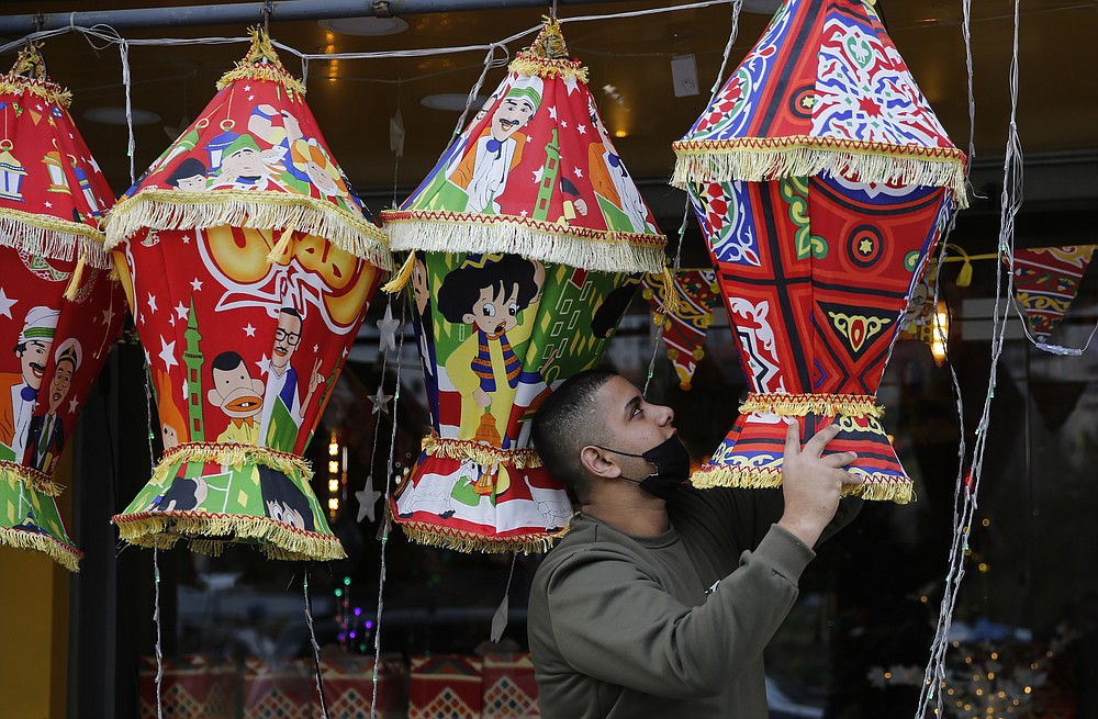 FILE - In this April 10, 2021, file photo, a Palestinian shopkeeper hangs Ramadan lanterns ahead of the Muslim fasting month of Ramadan, in the West Bank city of Nablus. Muslims are facing their second Ramadan in the shadow of the pandemic. Many Muslim majority countries have been hit by an intense new coronavirus wave. While some countries imposed new Ramadan restrictions, concern is high that the month’s rituals could stoke a further surge. (AP Photo/Majdi Mohammed, File)