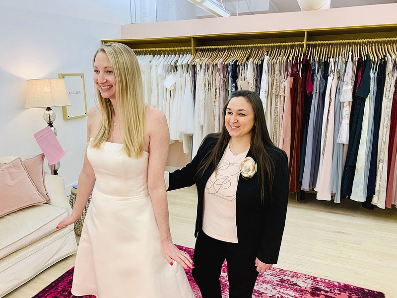 In this photo provided by Gilded Social, a bridal shop in Columbus, Ohio, owner Tanya Rutner Hartman helps customer Cristin Lee try on a gown at the shop on April 2, 2021. Although weddings and other big celebrations are going back on the calendar in the U.S., business owners who make those events happen expect a slow recovery from the impact of COVID-19. Hartman sees a shift in how couples feel about weddings, a change that can affect other businesses in the events industry as well. (Gilded Social via AP)