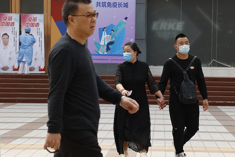 Chinese residents, some wearing masks, pass by a coronavirus vaccination center in Beijing  Friday, April 9, 2021. In a rare admission of the weakness of Chinese coronavirus vaccines, the country's top disease control official says their effectiveness is low and the government is considering mixing them to give them a boost. (AP Photo/Ng Han Guan)