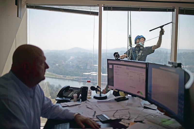 David Moon, owner of Moon Capital Management, works in his office as Scott Murrin cleans the windows on the 21st floor of Riverview Tower in downtown Knoxville, Tenn., Tuesday, April 6, 2021. Cleaning the 24-story tower takes around five days on average said Murrin, who has cleaned the building over 50 times in his career. (Calvin Mattheis/Knoxville News Sentinel via AP)