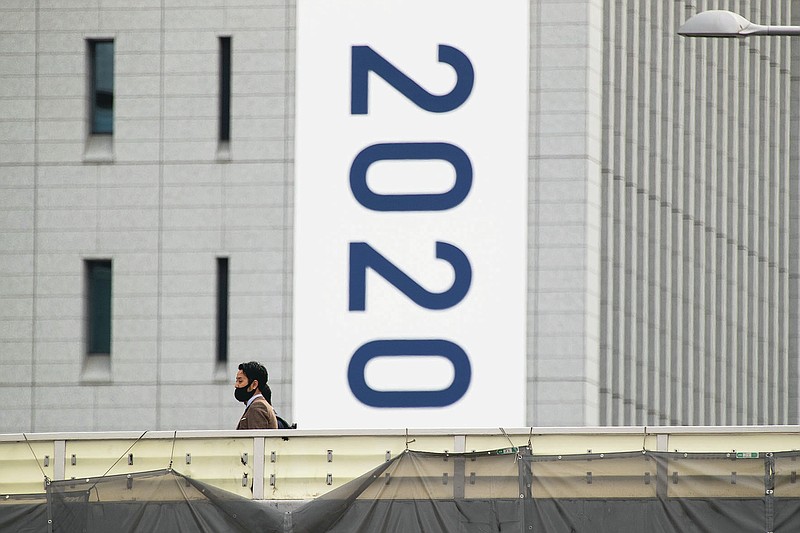 People wearing face masks walk on a crossover bridge near a banner to promote the rescheduled Tokyo 2020 Olympic Games in Tokyo Friday, April 2, 2021. Many preparations are still up in the air as organizers try to figure out how to hold the postponed games in the middle of a pandemic. (AP Photo/Hiro Komae)