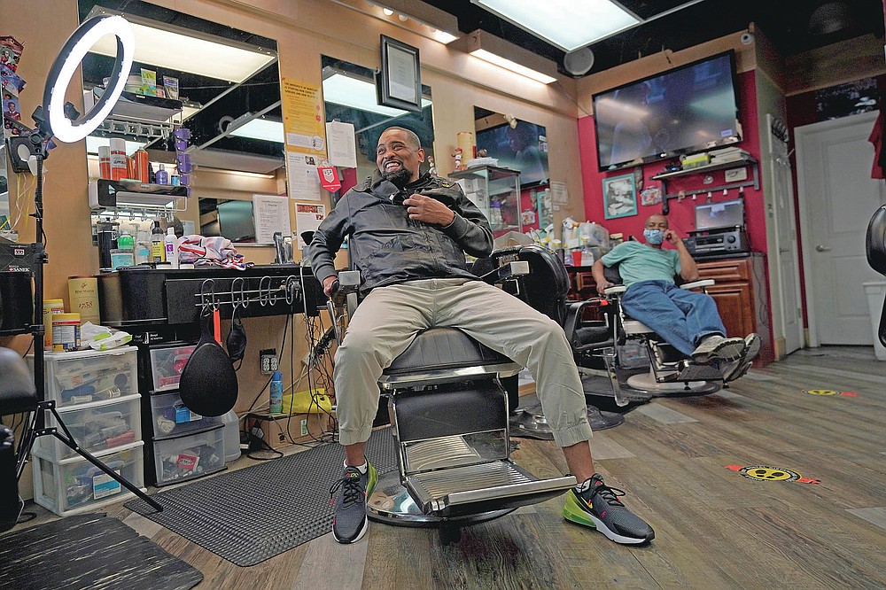 Mike Brown, a barber and health advocate, reacts while talking with colleagues and customers, Friday, April 9, 2021, in Hyattsville, Md. Brown is a member of the Health Advocates In Reach & Research (HAIR) program, which helps barbers and hair stylists to get certified to talk to community members about health. During the COVID-19 pandemic, Brown and a team of certified barbers have been providing factual information to customers about vaccines, a topic that historically has not been trusted by members of black communities because of the health abuse the race has endured over the years. (AP Photo/Julio Cortez)