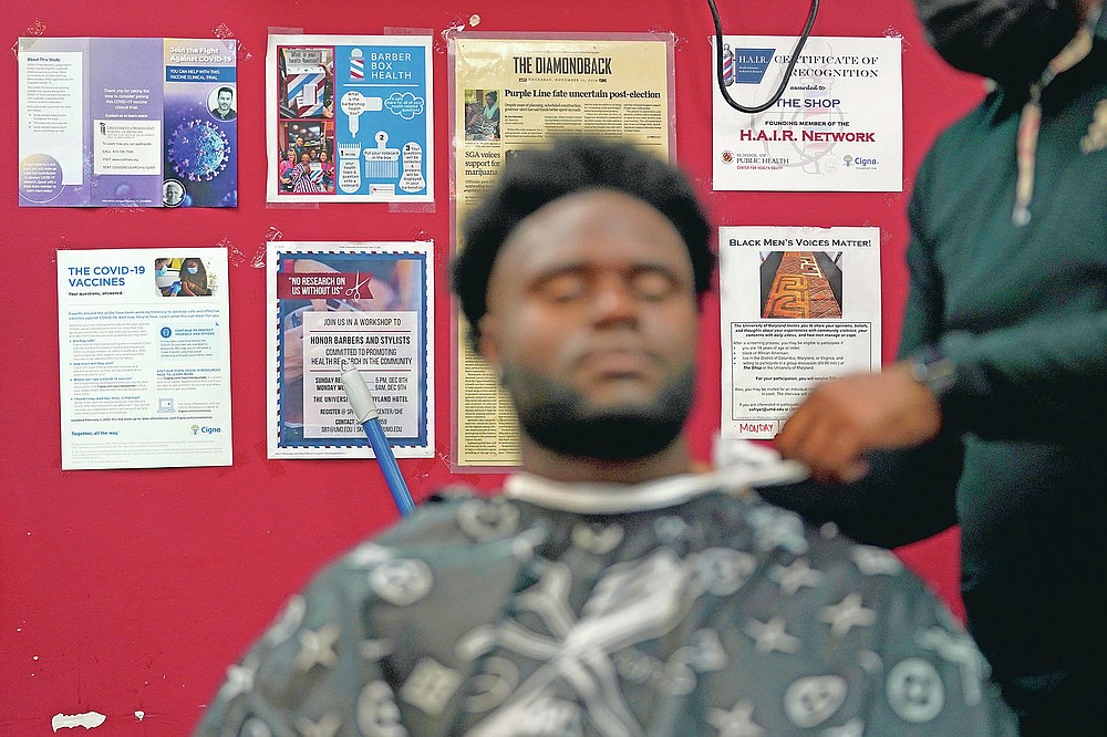 Health literature and a certificate are displayed on the wall as a patron gets a hair cut, Friday, April 9, 2021, in Hyattsville, Md. Barbers at The Shop are members of the Health Advocates In Reach & Research (HAIR) program, which helps barbers and hair stylists to get certified to talk to community members about health. During the COVID-19 pandemic, a team of certified barbers have been providing factual information to customers about vaccines, a topic that historically has not been trusted by members of black communities because of the health abuse the race has endured over the years. (AP Photo/Julio Cortez)