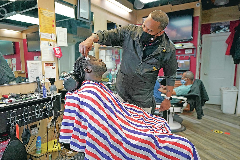 Mike Brown, right, a barber and health advocate, lines up the facial hair of Vyron Cox Jr., Friday, April 9, 2021, in Hyattsville, Md. Brown is a member of the Health Advocates In Reach & Research (HAIR) program, which helps barbers and hair stylists to get certified to talk to community members about health. During the COVID-19 pandemic, Brown and a team of certified barbers have been providing factual information to customers about vaccines, a topic that historically has not been trusted by members of black communities because of the health abuse the race has endured over the years. (AP Photo/Julio Cortez)