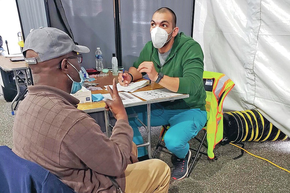 In this March 12, 2021 photo provided by Unity Health Care, Othon Sosua, right, talks with a patient during a vaccination drive in Washington, D.C. Homeless Americans who have been left off priority lists for coronavirus vaccinations β or even bumped aside as states shifted eligibility to older age groups β are finally getting their shots as vaccine supplies increase. Walk-up vaccine events are crucial for a population with limited access to cars, cellphones or Wi-Fi, organizers say. (Unity Health Care via AP)
