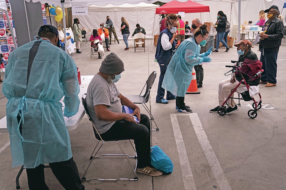 FILE - In this Feb. 10, 2021, file photo, Viola Roberson, 75, far right, and 61-year-old Mark McNamee, foreground, wait for their COVID-19 vaccine at a vaccination site set up in the parking lot of the Los Angeles Mission in the Skid Row area of Los Angeles. While older homeless adults were eligible for vaccination in many states earlier this year, the shots now are finally reaching thousands of younger adults who are homeless. (AP Photo/Jae C. Hong, File)