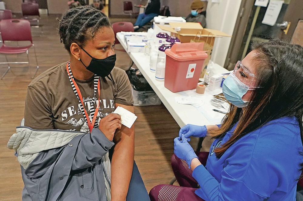 Judy Jideonwo, left, a case manager at Angeline's Day Center For Women, which is part of a YWCA shelter for women lacking housing in Seattle, holds her vaccination card after she received the first dose of the Moderna COVID-19 vaccine, Wednesday, April 7, 2021, from Aurora Artman, right, a medical assistant at Harborview Medical Center, at a vaccination clinic set up at the shelter. Advocates say homeless people are at greater risk of being infected and greater risk of hospitalization and death than the average person, and they should have been prioritized earlier. (AP Photo/Ted S. Warren)